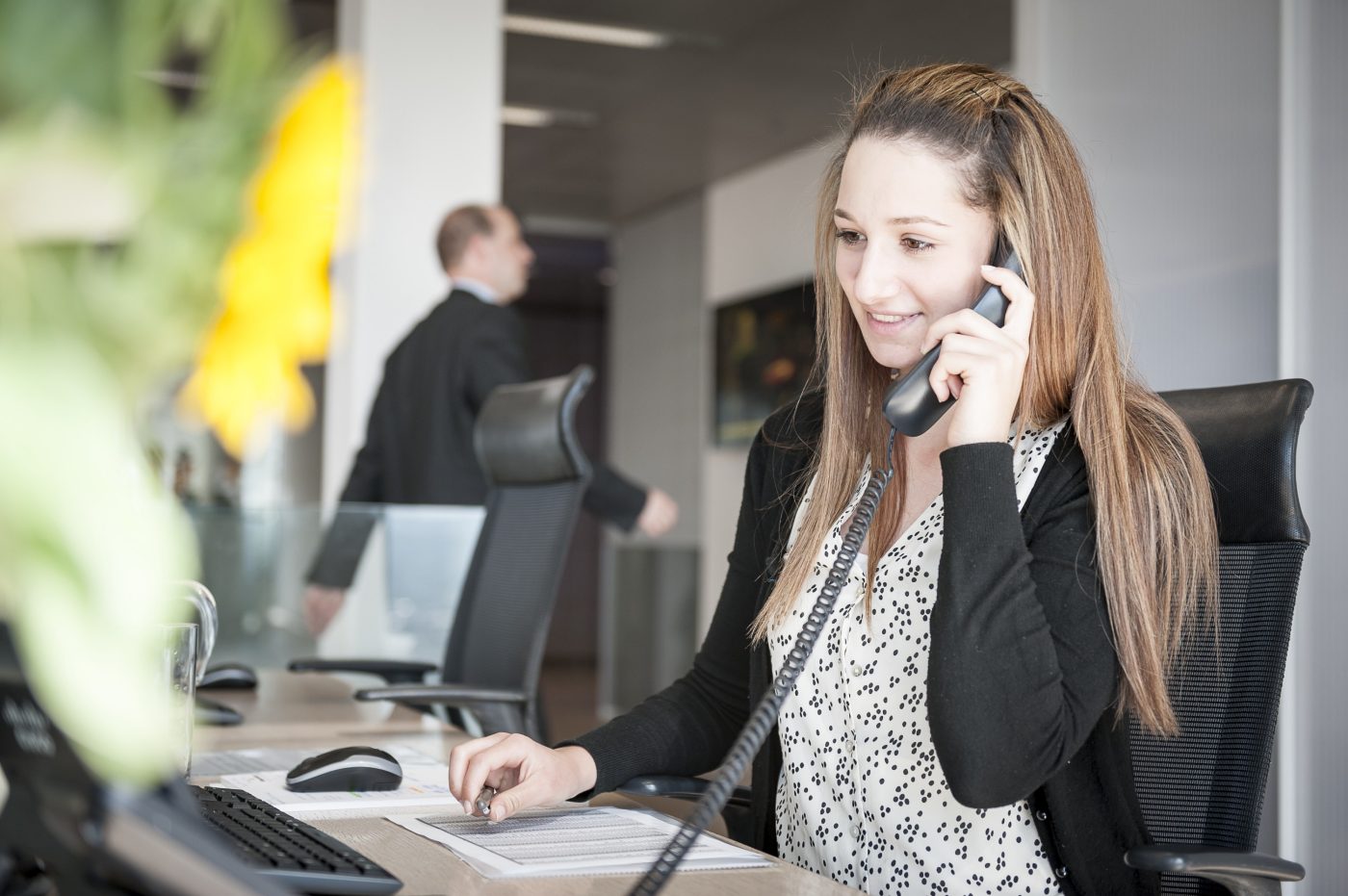 Young woman at reception desk holding telephone.