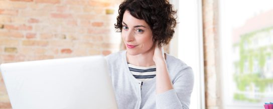 Woman looking at computer screen in front of brick-lined wall