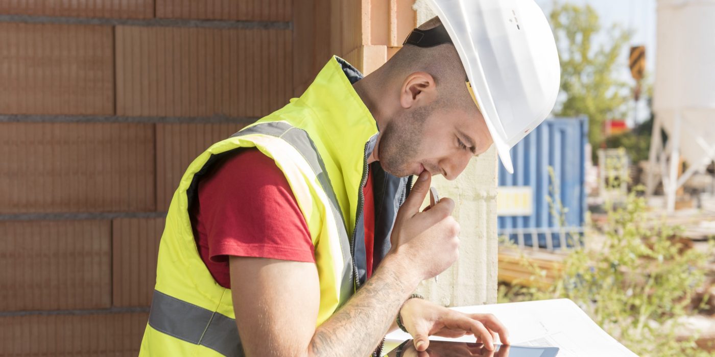 Construction worker working with tablet placed on blueprint in building shell