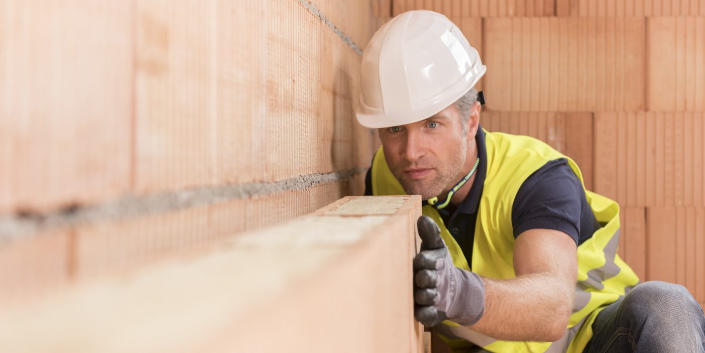 Construction worker checking alignment of mineral-wool filled clay block