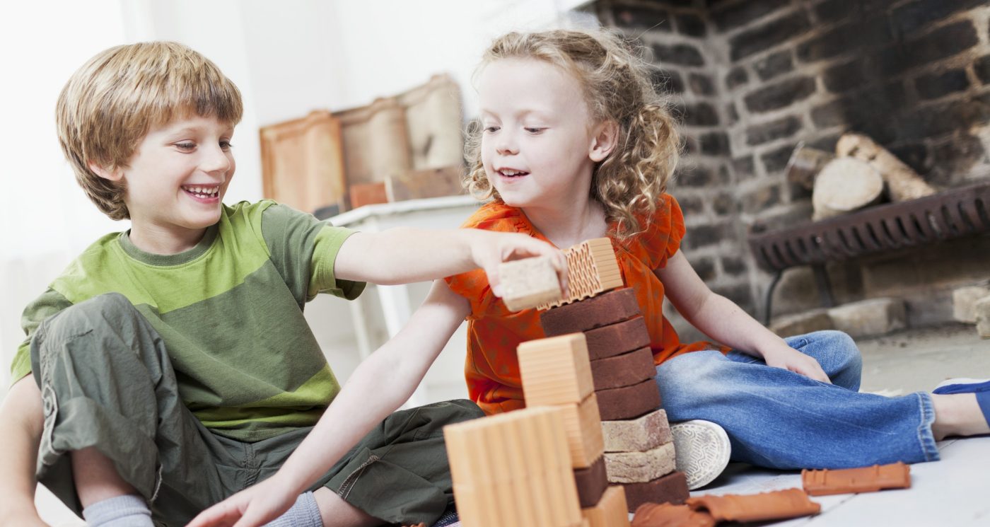Boy and girl playing with miniature bricks, clay blocks and clay roof tiles in front of fireplace