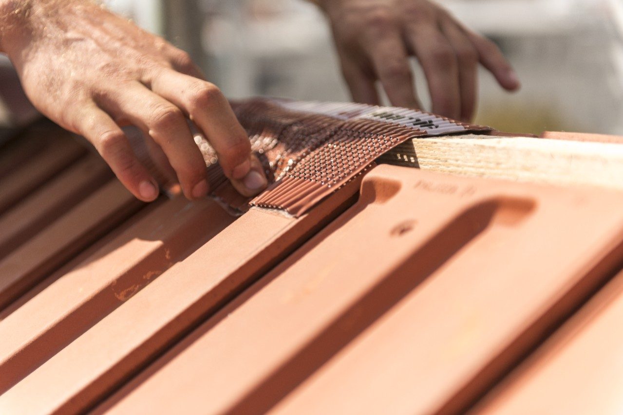 Roofer applying Alu-Grip Rol ridge and hip roll on ridge with bare hands