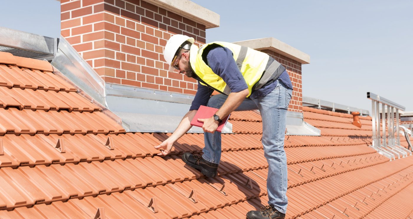 Product manager checking ventilation roof tiles in front of chimney standing on the roof wearing hard hat and safety jacket