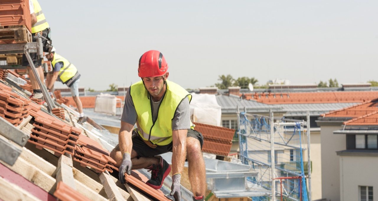 Urban roofers at work wearing safety jacket and hard hat laying roof tiles at an urban location