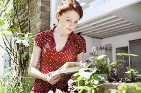 Woman reading a book next to open window in front of brick wall