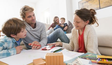 Father with two kids sketching and mother with boy reading a book in living room