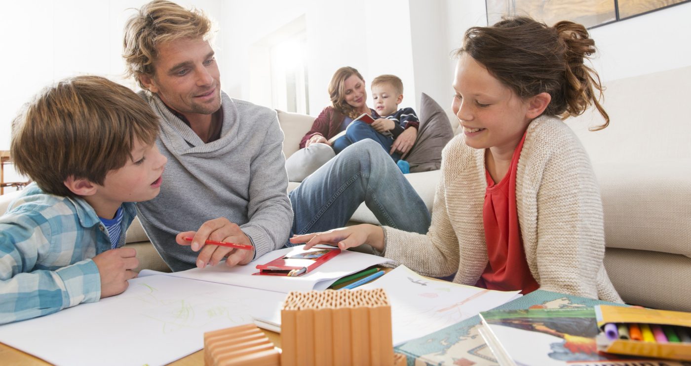Father with two kids sketching and mother with boy reading a book in living room