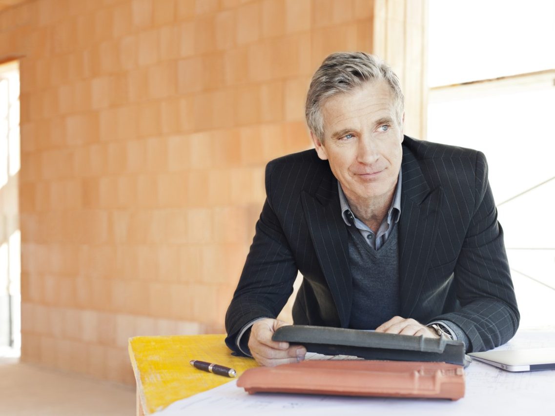 Man in suit comparing roof tiles in unfinished building surrounded by bare brickwork
