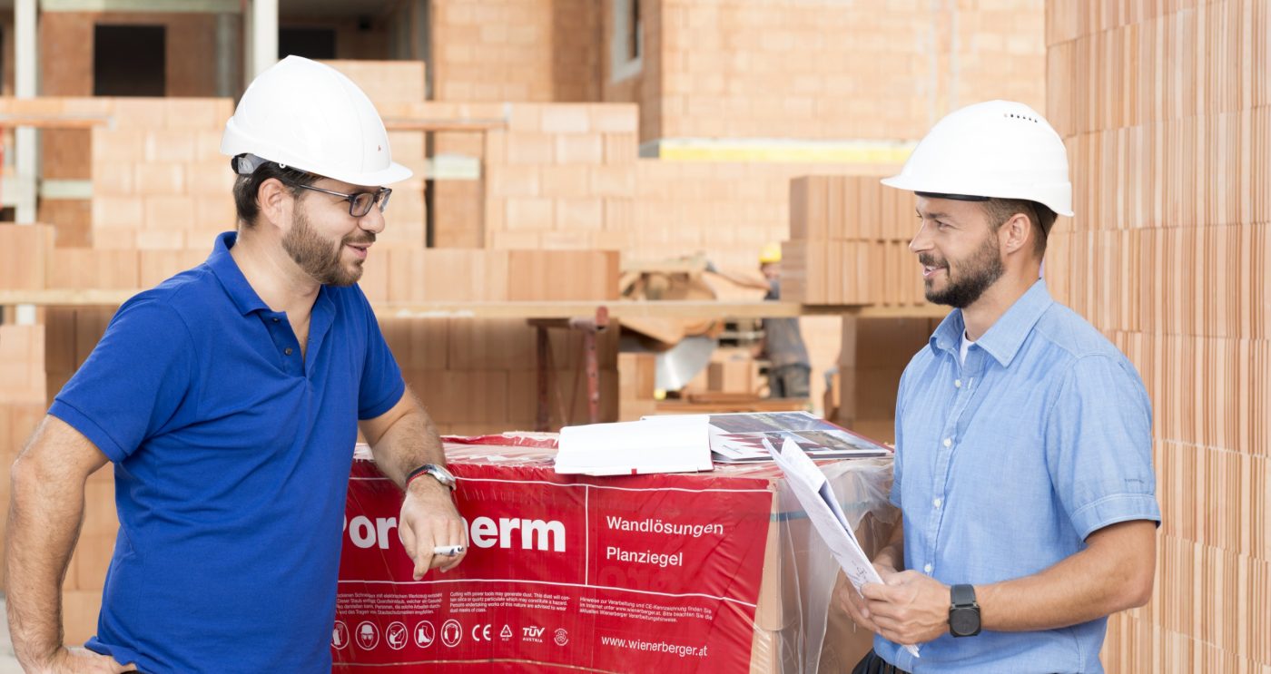 Building professionals talking at construction site next to foil wrapped pallette of brick blocks. > There is another version of this image available with another worker in the background